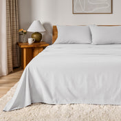 A bed dressed in flannel sheet set in a bedroom with a wooden headboard, bedside table and lamp