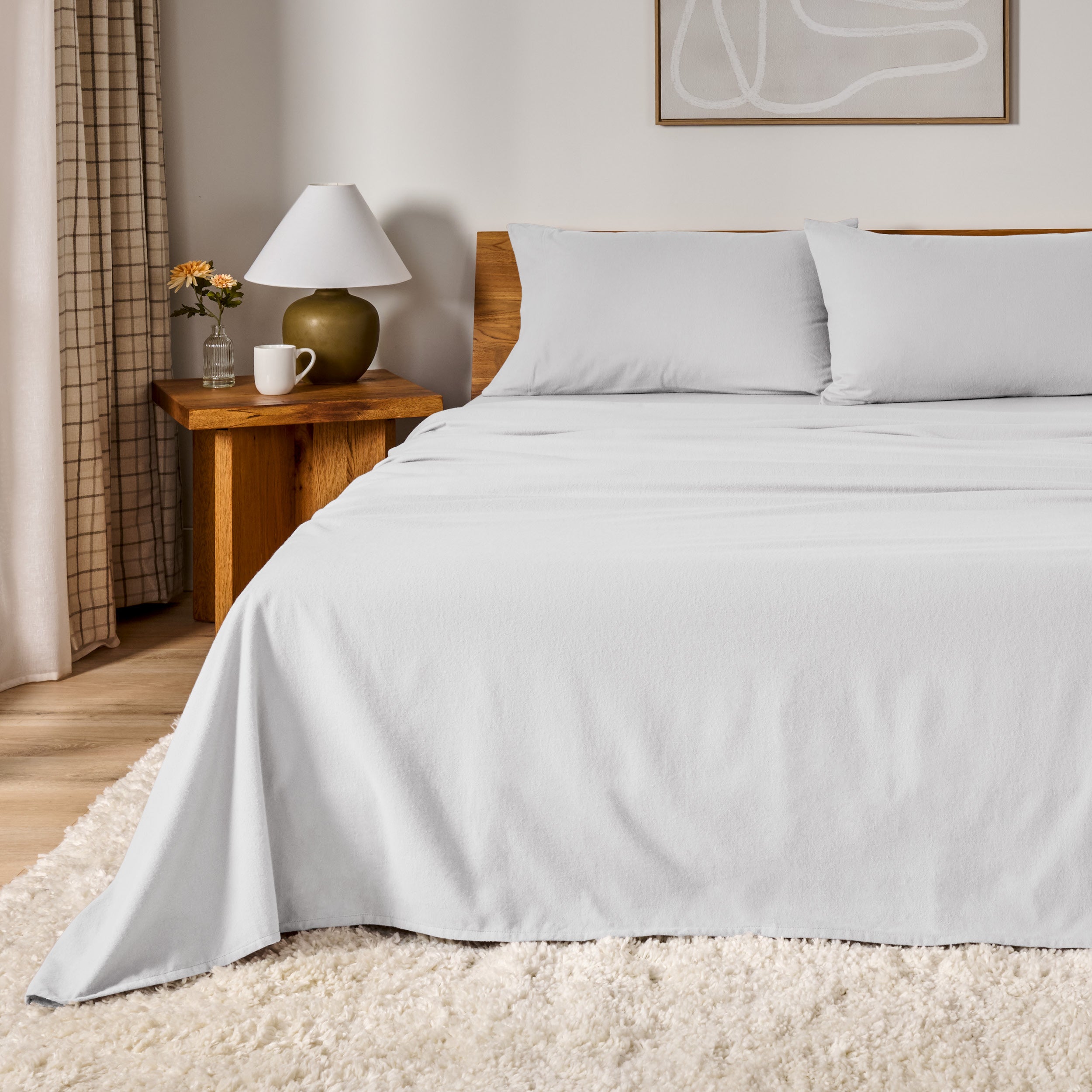 A bed dressed in flannel sheet set in a bedroom with a wooden headboard, bedside table and lamp