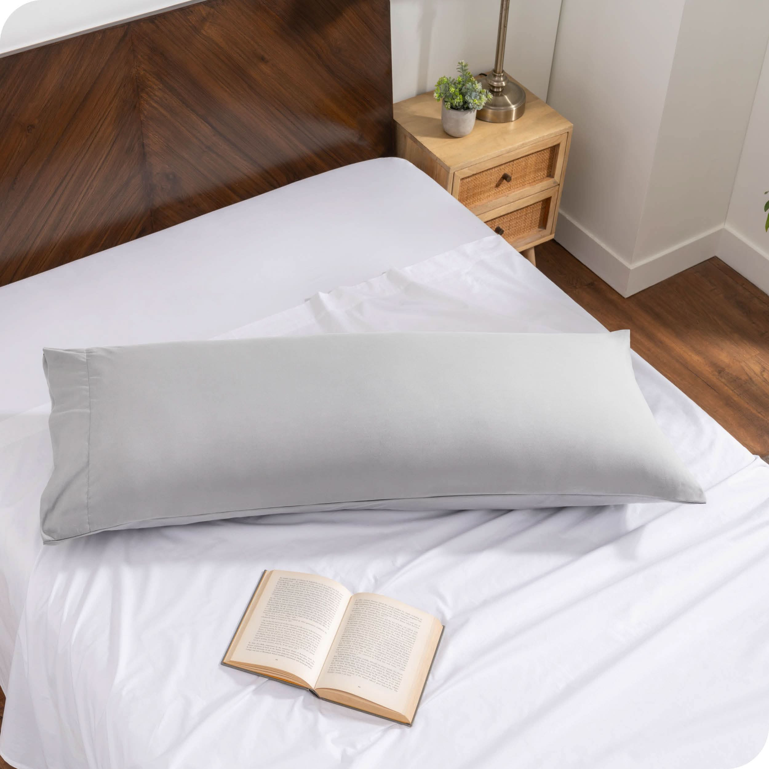 A body pillow cover on a pillow on a bed made with all white bedding