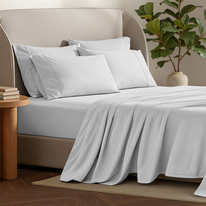 Bed sheets and pillows on a bed with a plant and side table in the background.