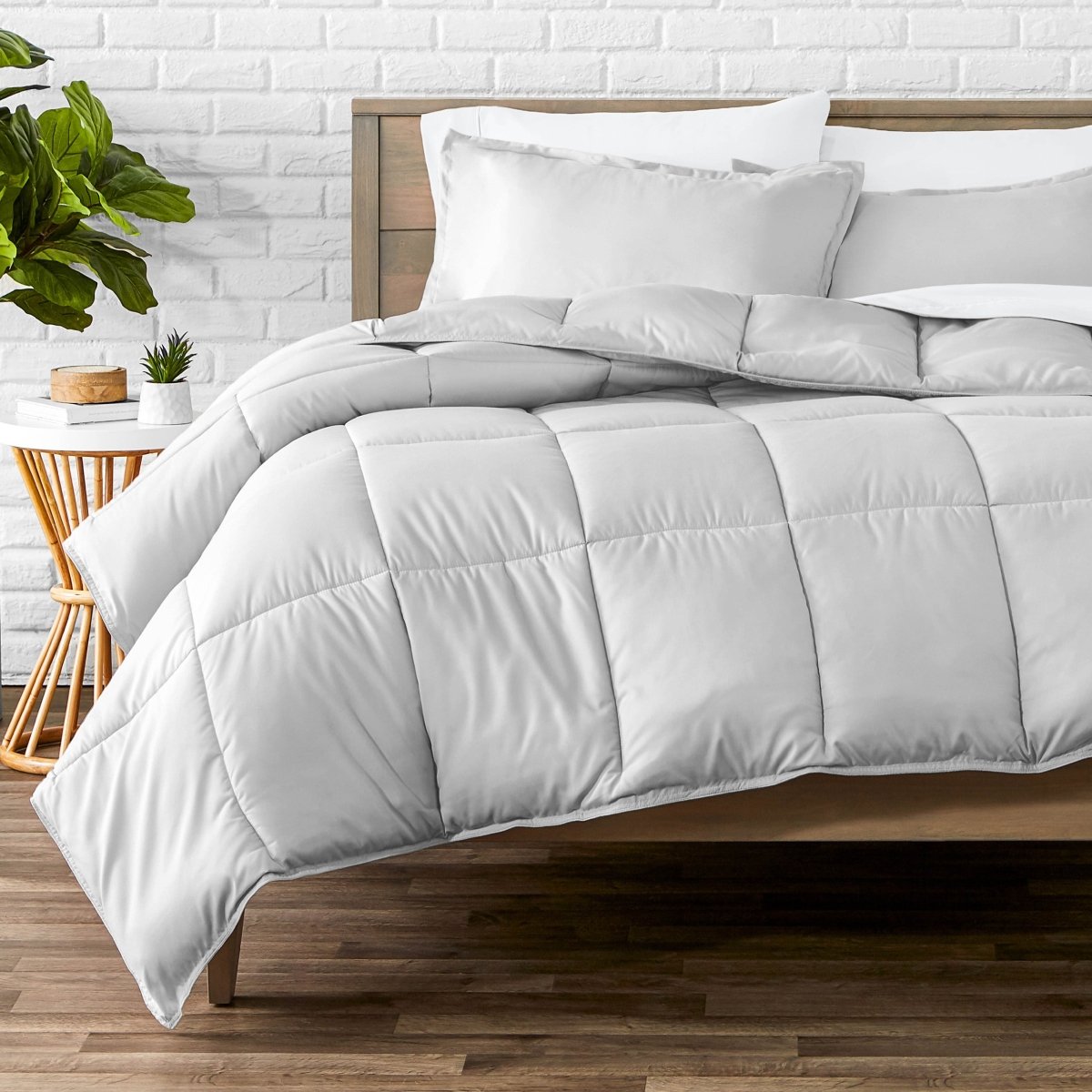 Comforter set on a bed with a white brick wall and plant in the background