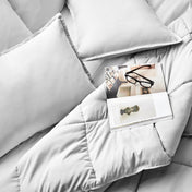 Comforter and pillows on a bed with a magazine and glasses.