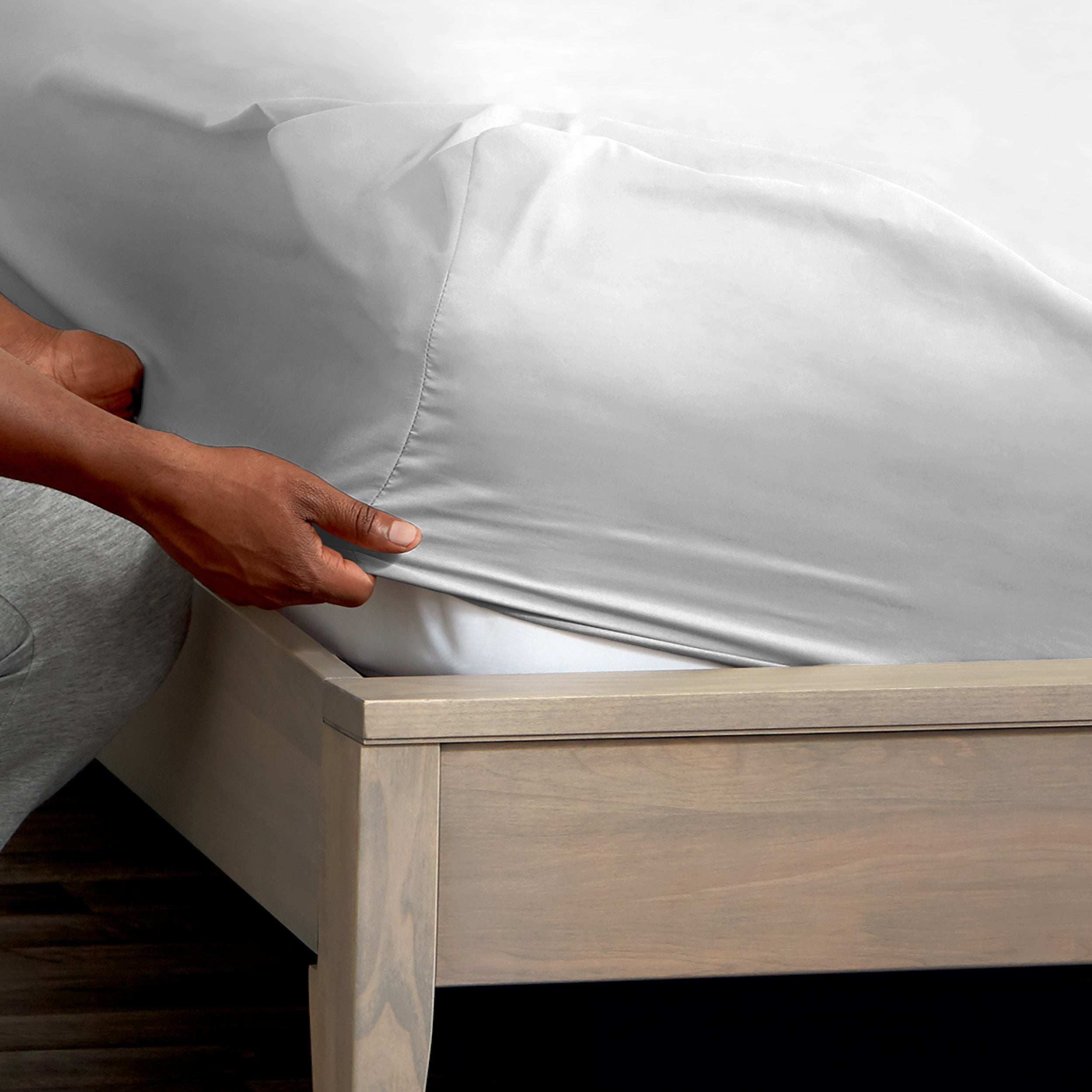 A man is putting a fitted sheet on a bed