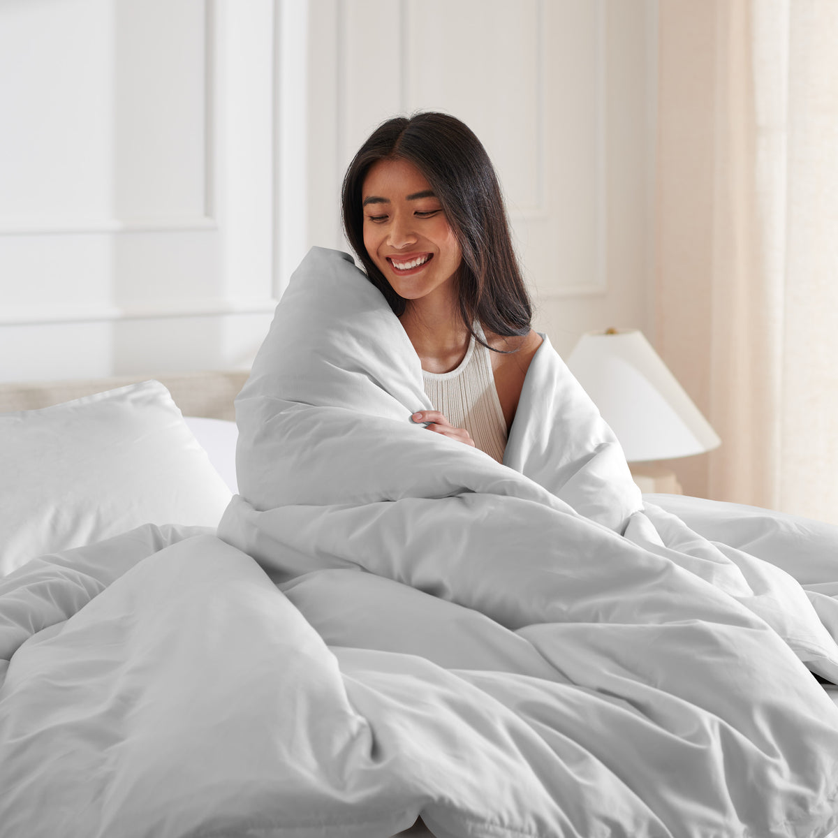 Woman smiling under duvet cover set in a bedroom setting