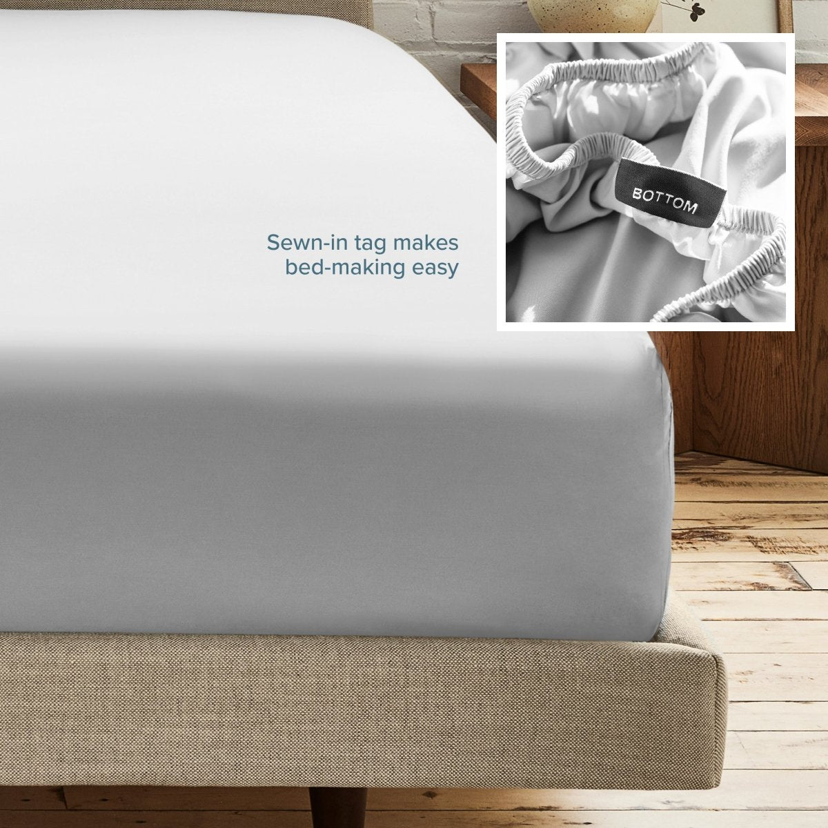 A fitted bed sheet on a bed frame with a small inset close-up of the elastic and a sewn-in tag labeled BOTTOM. White text on the sheet reads, 'Sewn-in tag makes bed-making easy.