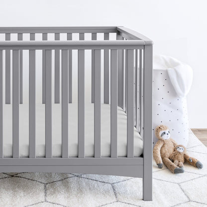 Gray crib with stuffed animals on the floor next to it