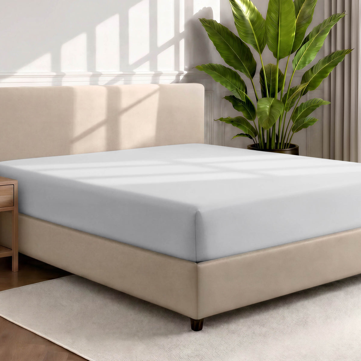 Bed with a fitted sheet in a room with a large plant and rug