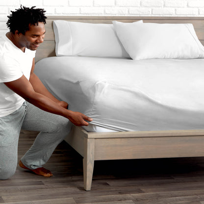 Man adjusting fitted sheet on a bed with white pillows.