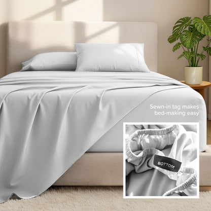 Bed sheets and pillows on a bed with a plant in the background