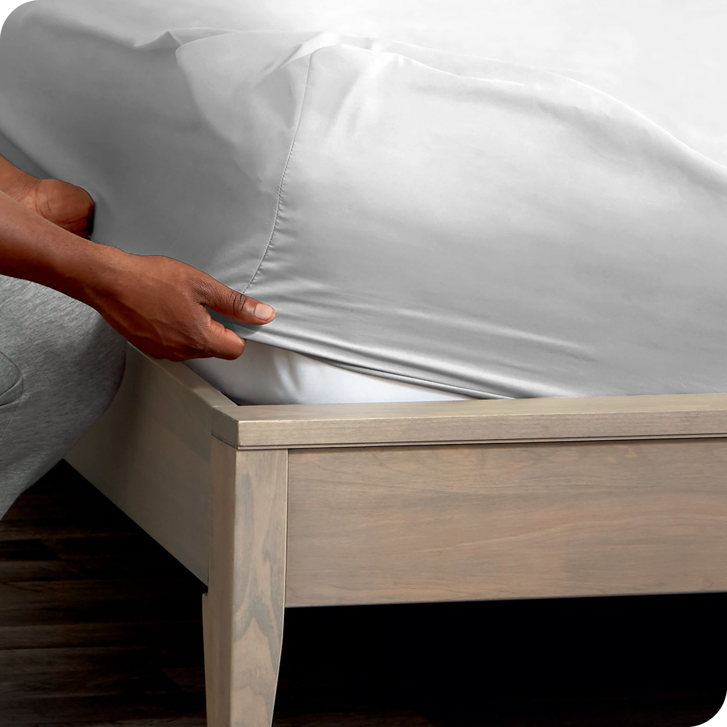 A man is putting a fitted sheet on a mattress