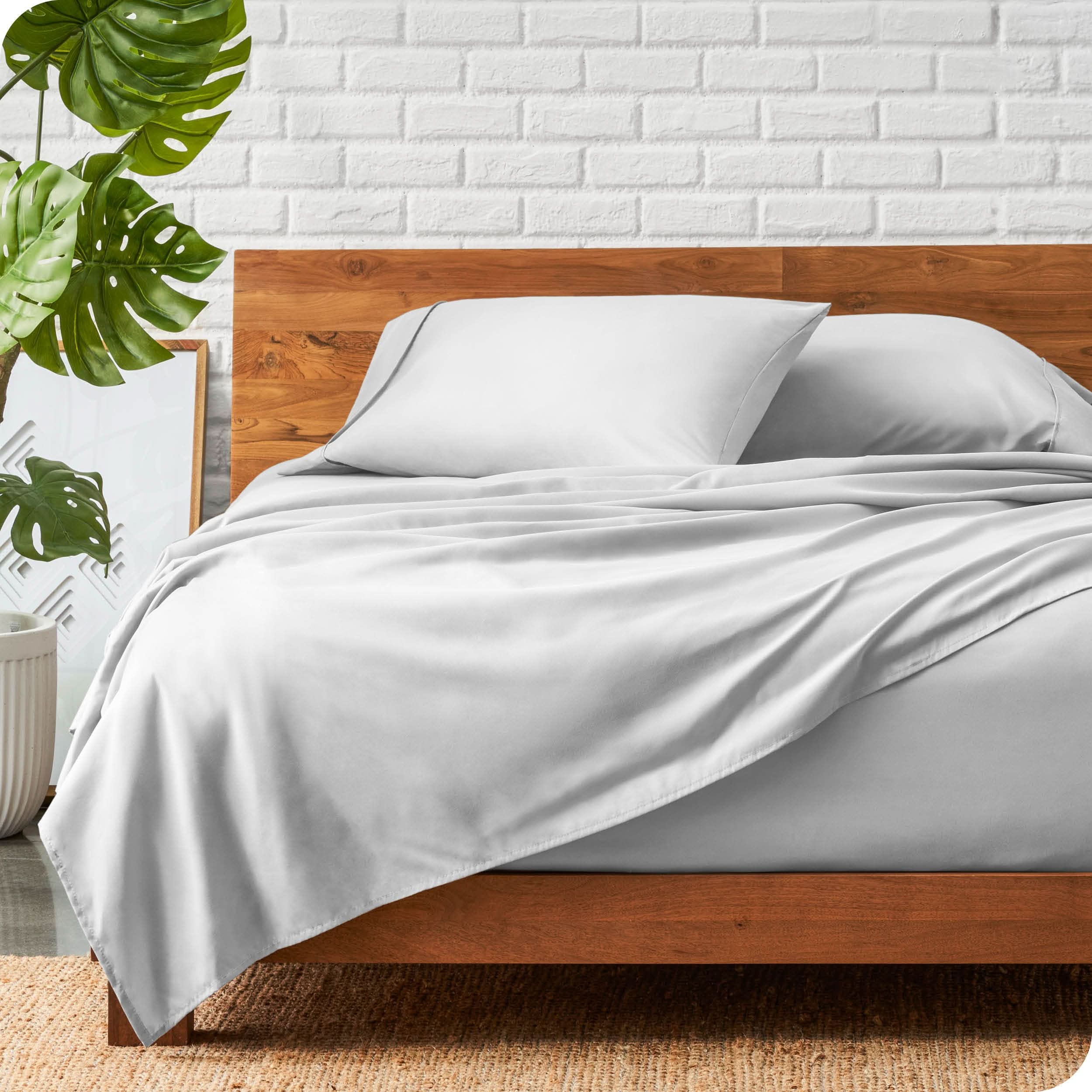 A wooden bed frame with a microfiber sheet set on the mattress.