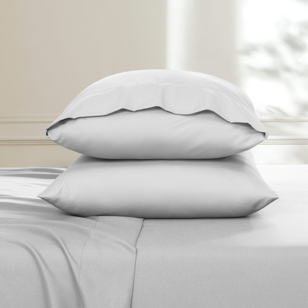 Two pillows stacked on a bed with a neutral background