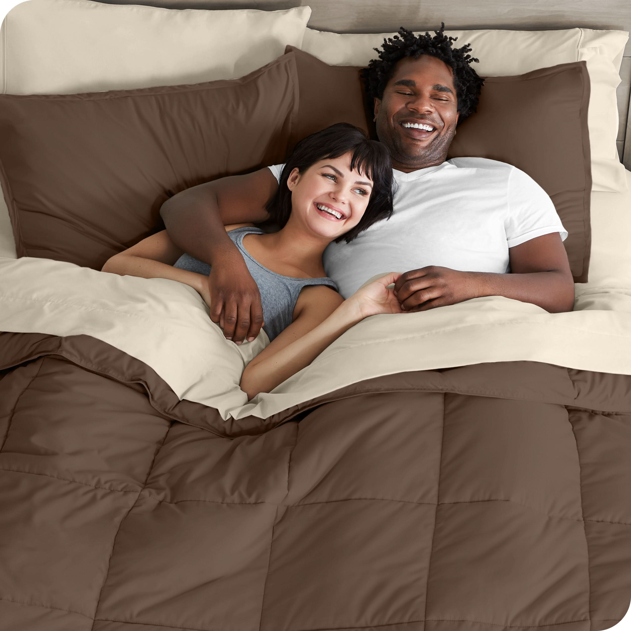 A couple is lying in bed with a comforter and sheets over them