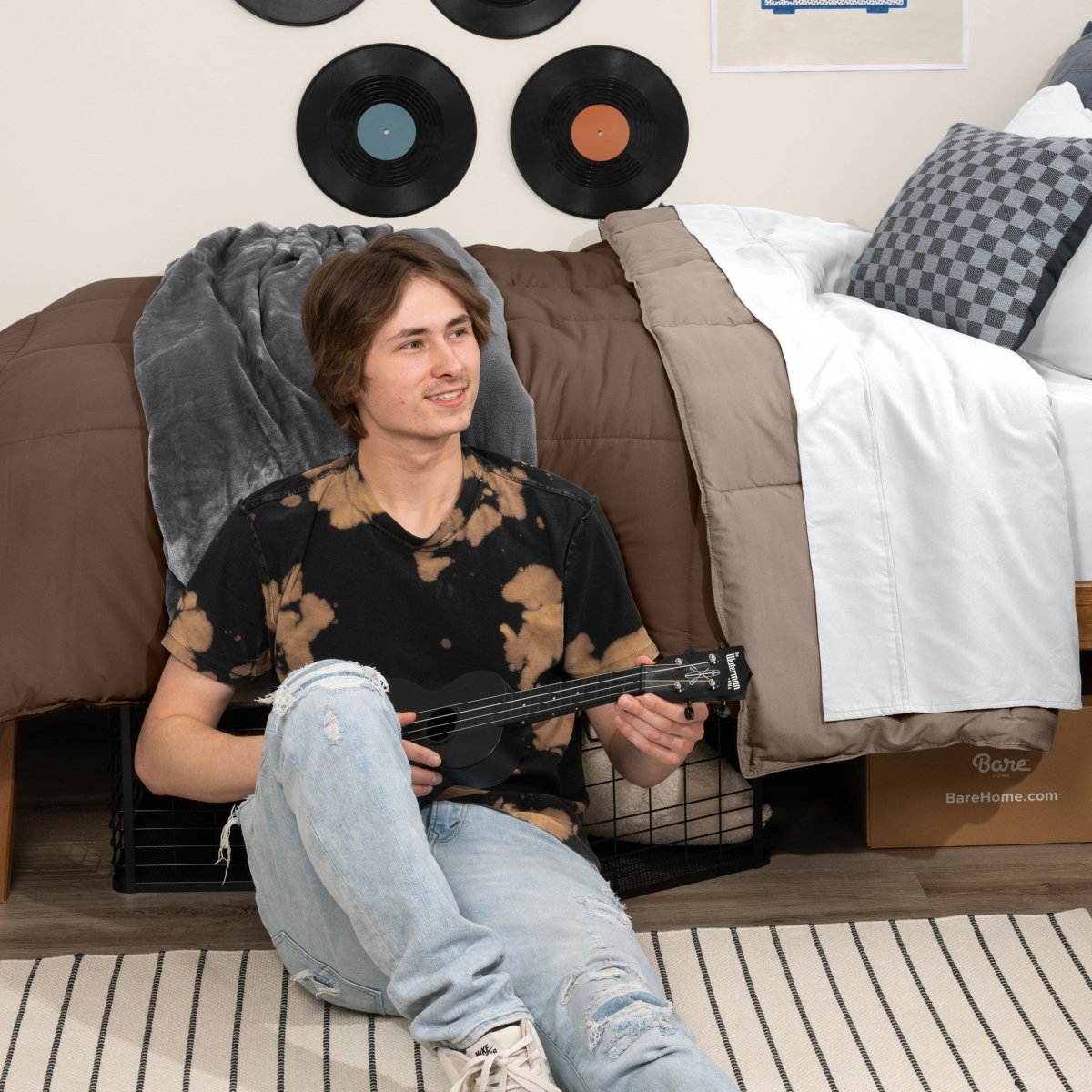 Person sitting on a bed holding a guitar in a bedroom setting with vinyl records on the wall.