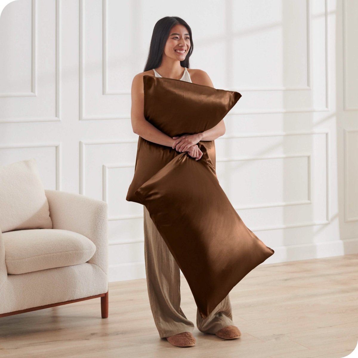 A woman standing while holding pillows with silk pillowcases on them