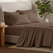 Bed sheets and pillows on a bed with a plant and side table in the background.