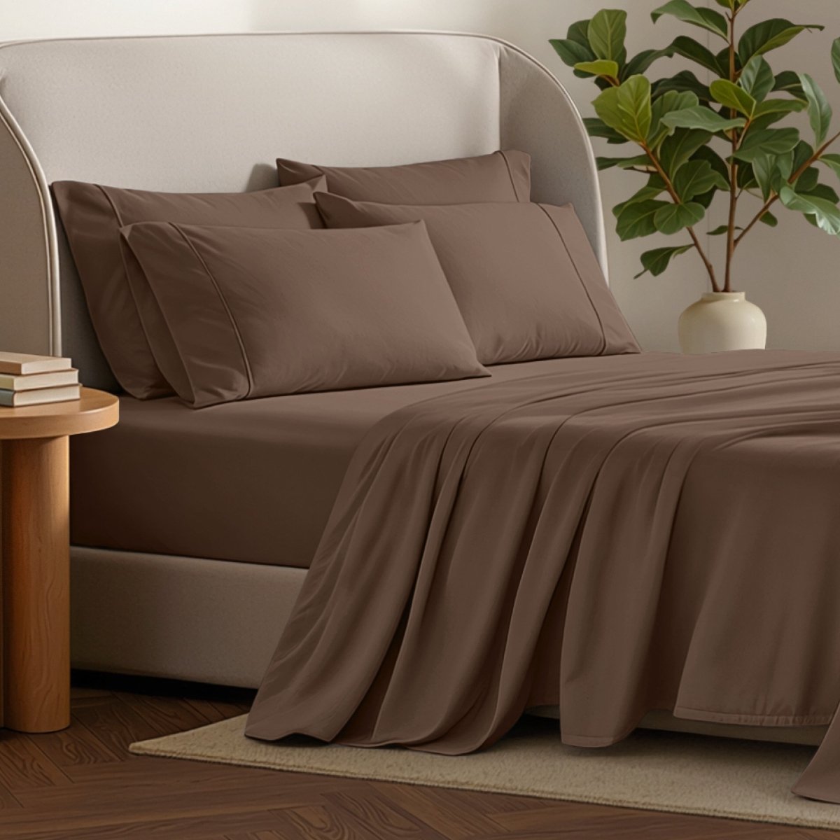 Bed sheets and pillows on a bed with a plant and side table in the background.