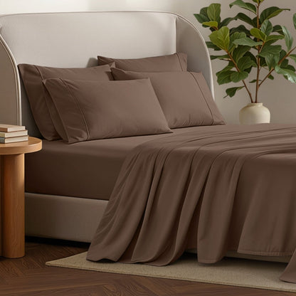 Bed sheets and pillows on a bed with a plant and side table in the background.