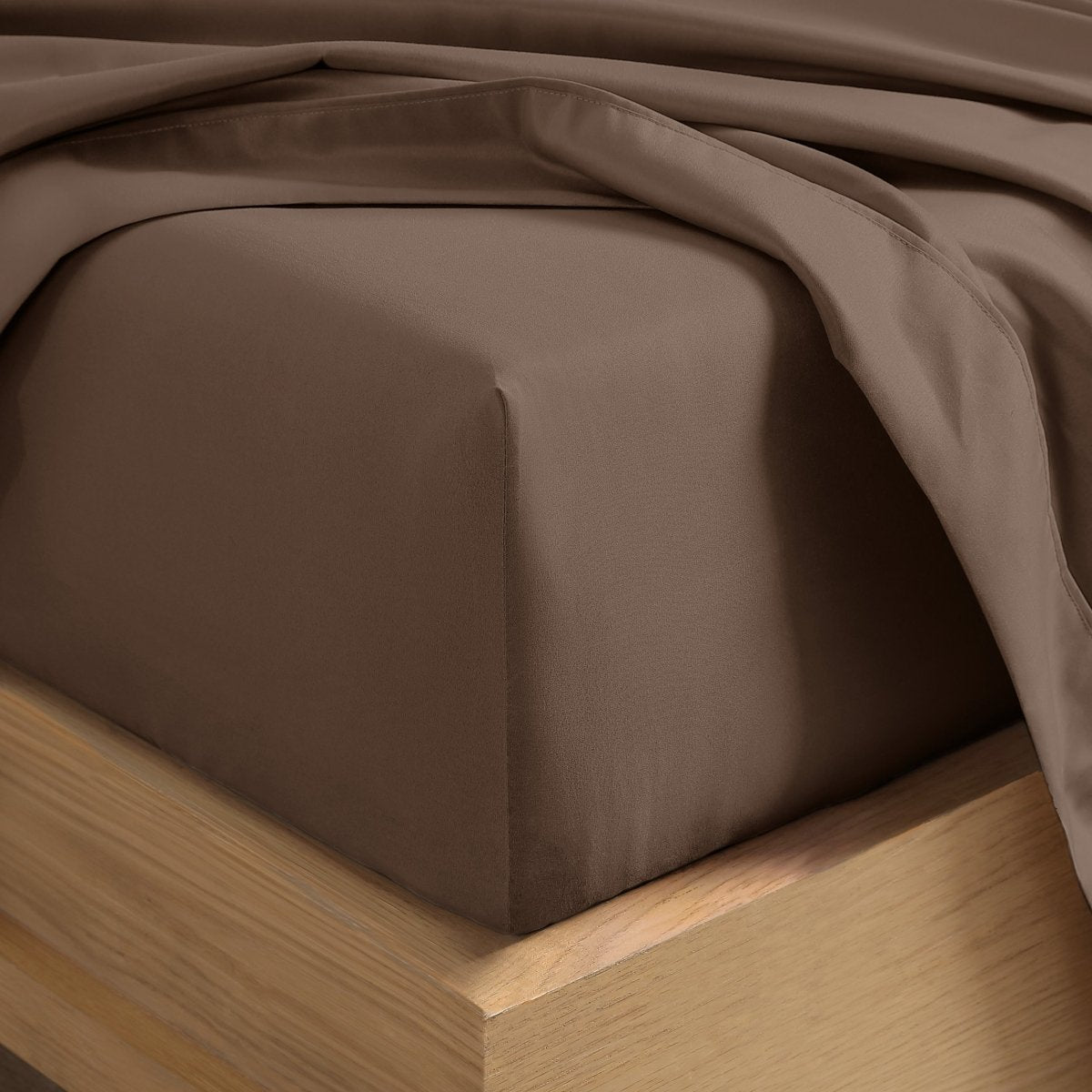 A close-up of a fitted sheet covering the corner of a bed frame, with matching top sheet draped over it.