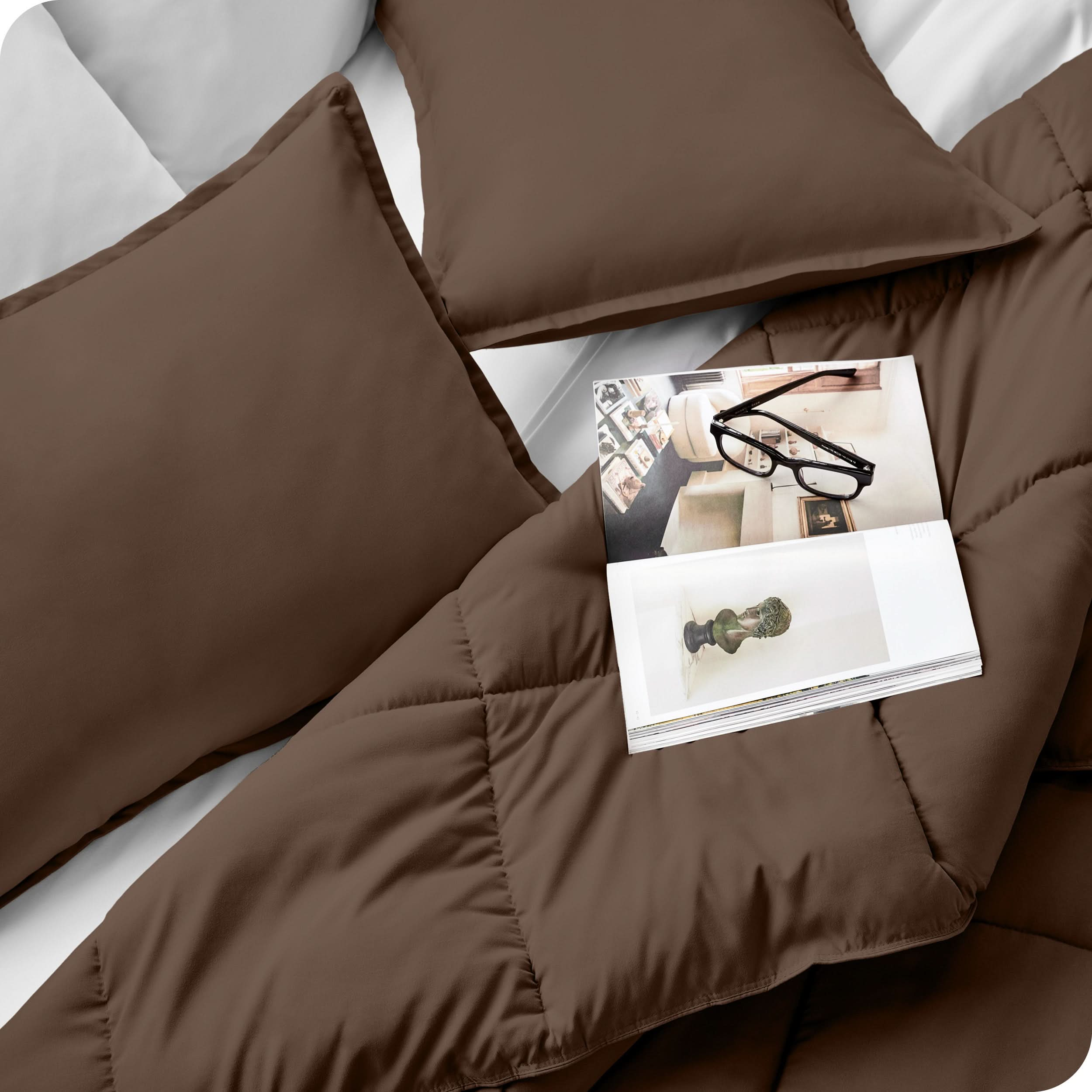 Close up of a comforter set on a bed. There are glasses and a magazine on top of the comforter.