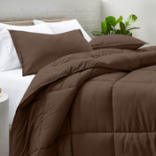 Comforter and pillow shams on a bed with a white brick wall and plant in the background