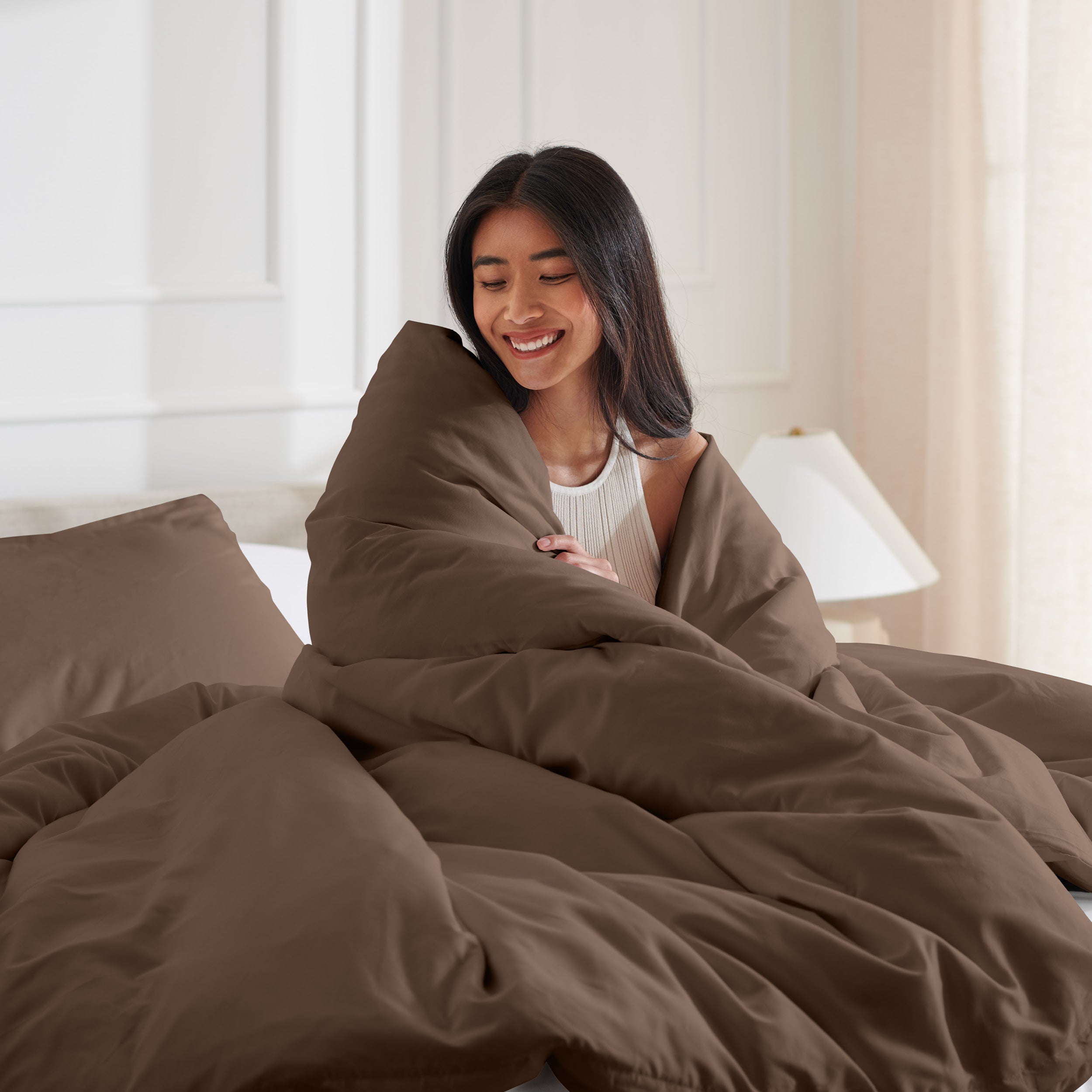 Woman smiling under duvet cover set in a bedroom setting