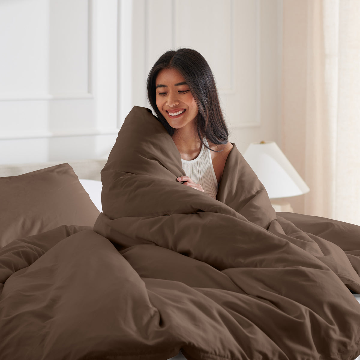 Woman smiling under duvet cover set in a bedroom setting