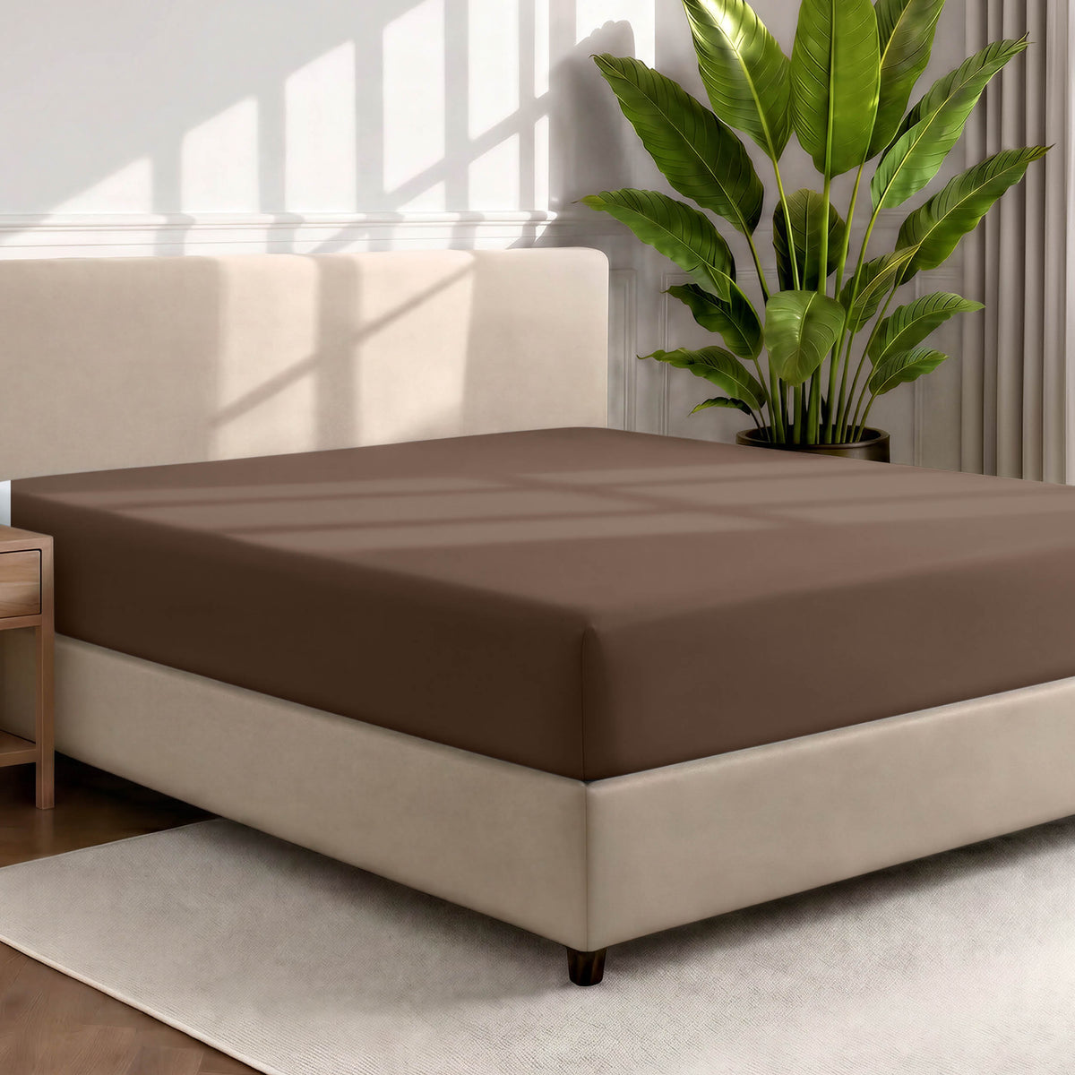 Bed with a fitted sheet in a room with a large plant and rug