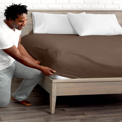 Man adjusting fitted sheet on a bed with white pillows.