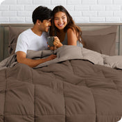 A couple sitting in a bed made with a reversible comforter and sheet set