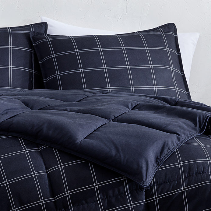 Midhnight blue checkered comforter and pillow on a bed with a light gray wall background