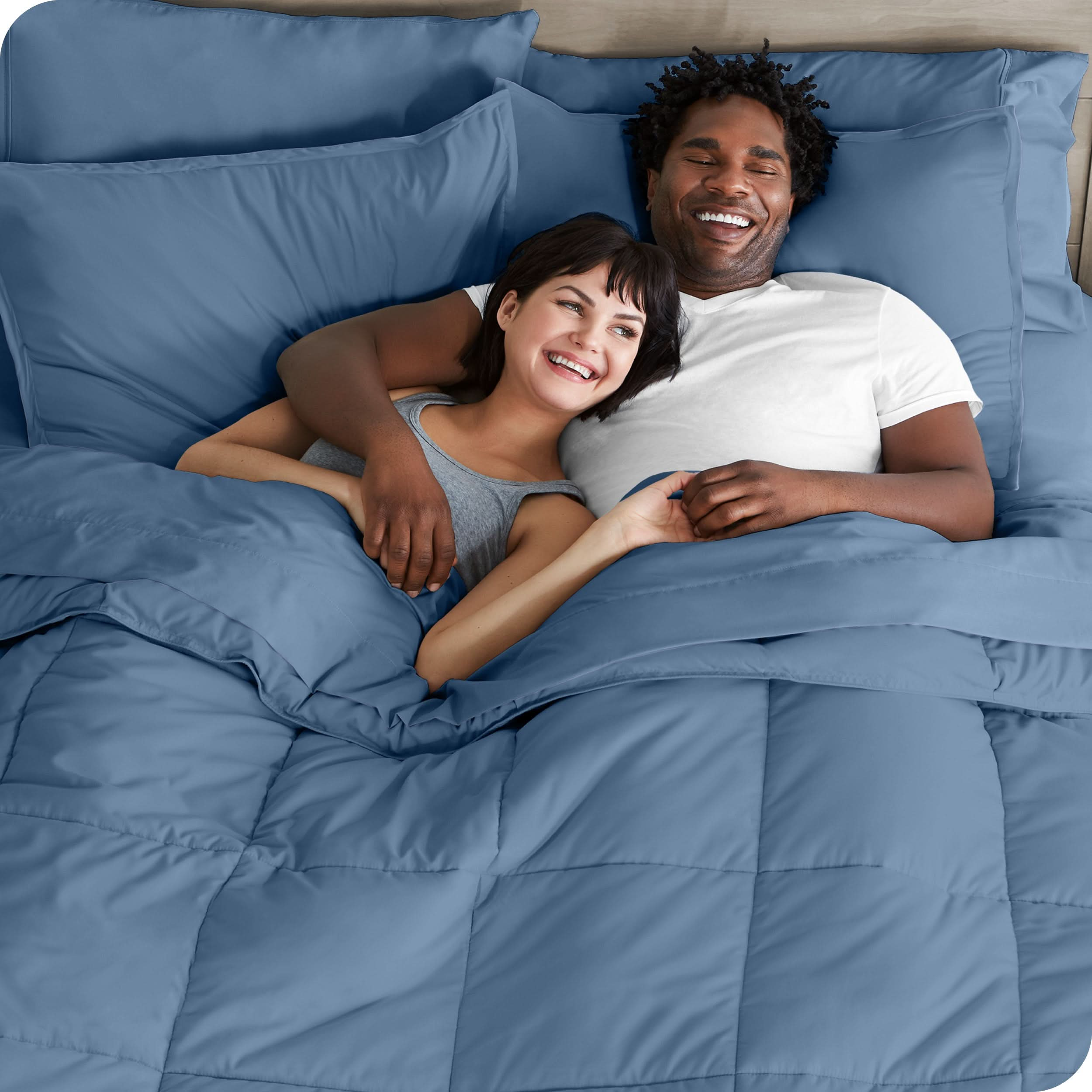 A couple is lying in bed with a comforter and sheets over them