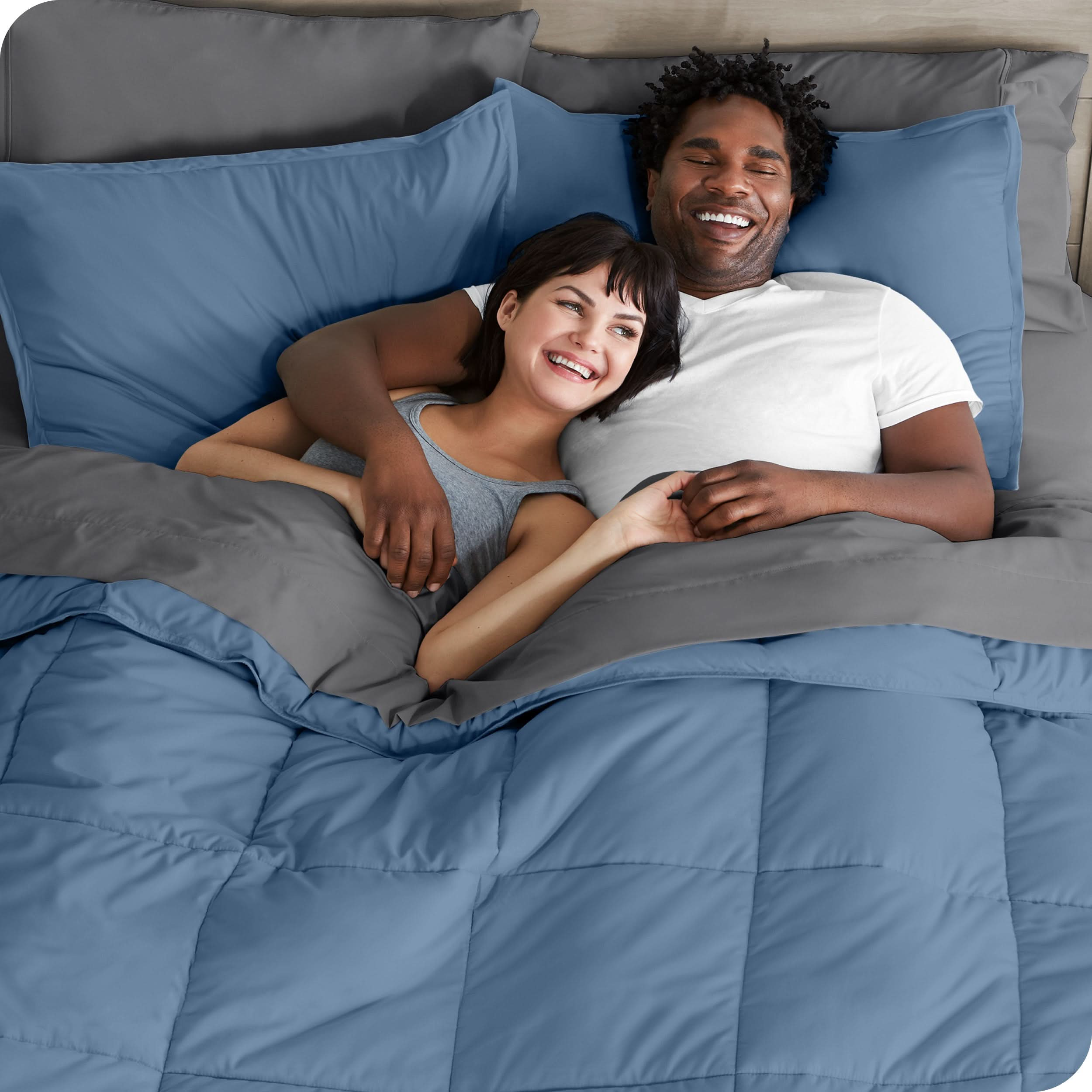 A couple is lying in bed with a comforter and sheets over them