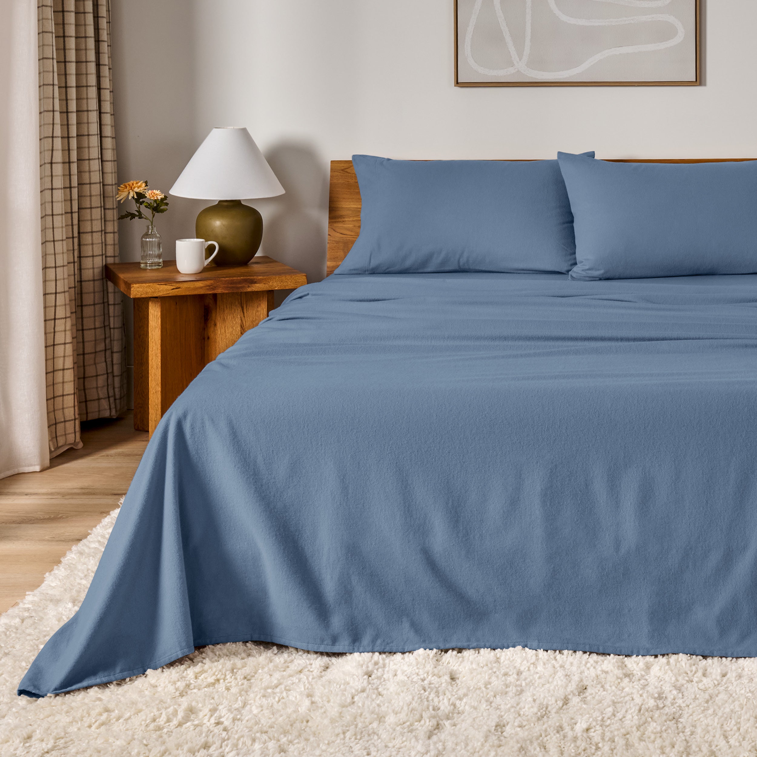 A bed dressed in flannel sheet set in a bedroom with a wooden headboard, bedside table and lamp