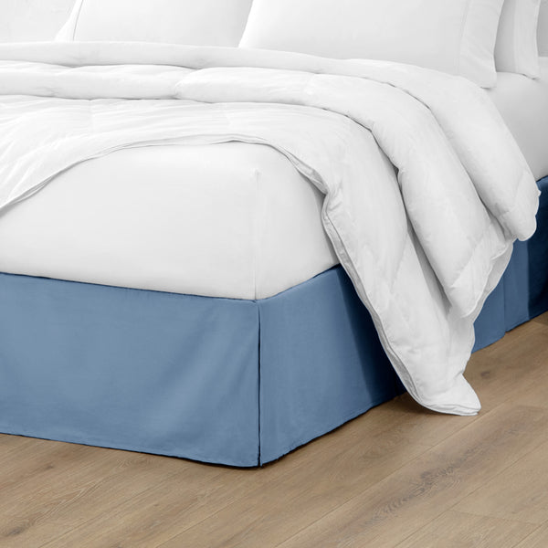 A modern bed with a microfiber bed skirt with pleats on the corners and midway on each side