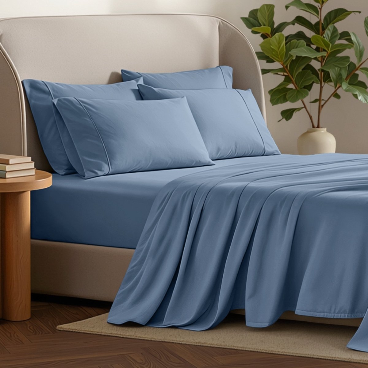 Bed sheets and pillows on a bed with a plant and side table in the background.