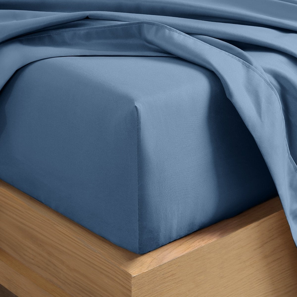 A close-up of a fitted sheet covering the corner of a bed frame, with matching top sheet draped over it.