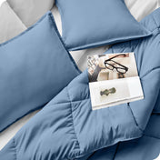 Close up of a comforter set on a bed. There are glasses and a magazine on top of the comforter.