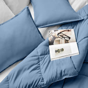 Comforter and pillows on a bed with a magazine and glasses.
