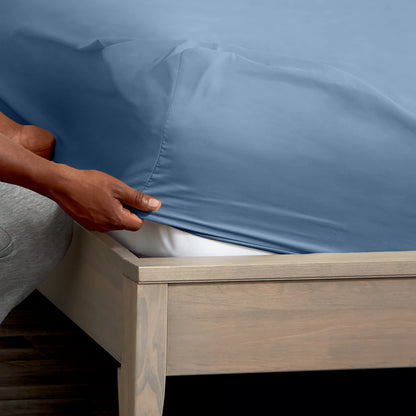A man is putting a fitted sheet on a bed