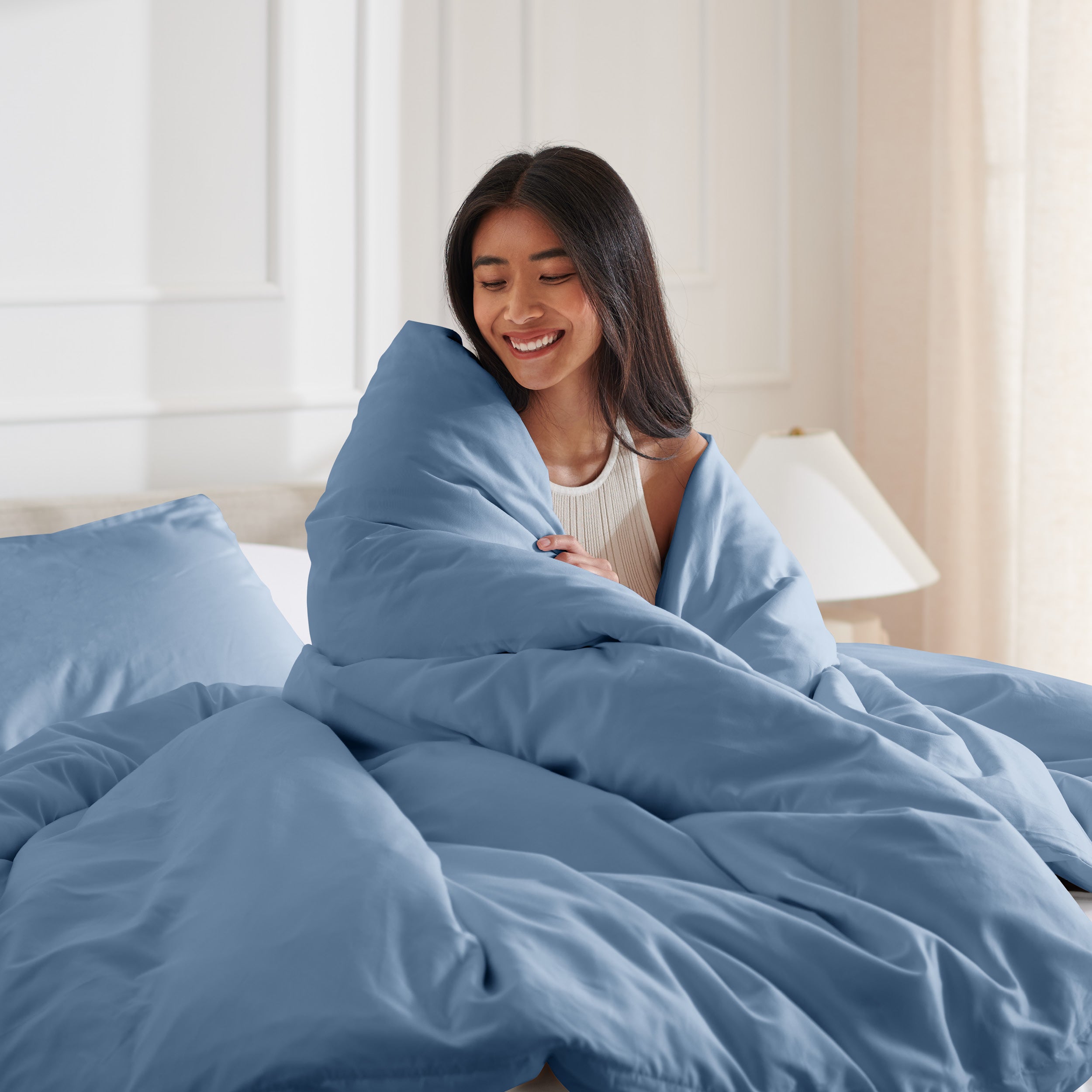 Woman smiling under duvet cover set in a bedroom setting