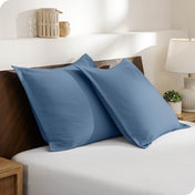 Two pillows with shams on a bed in a bedroom setting with a lamp and decor items.