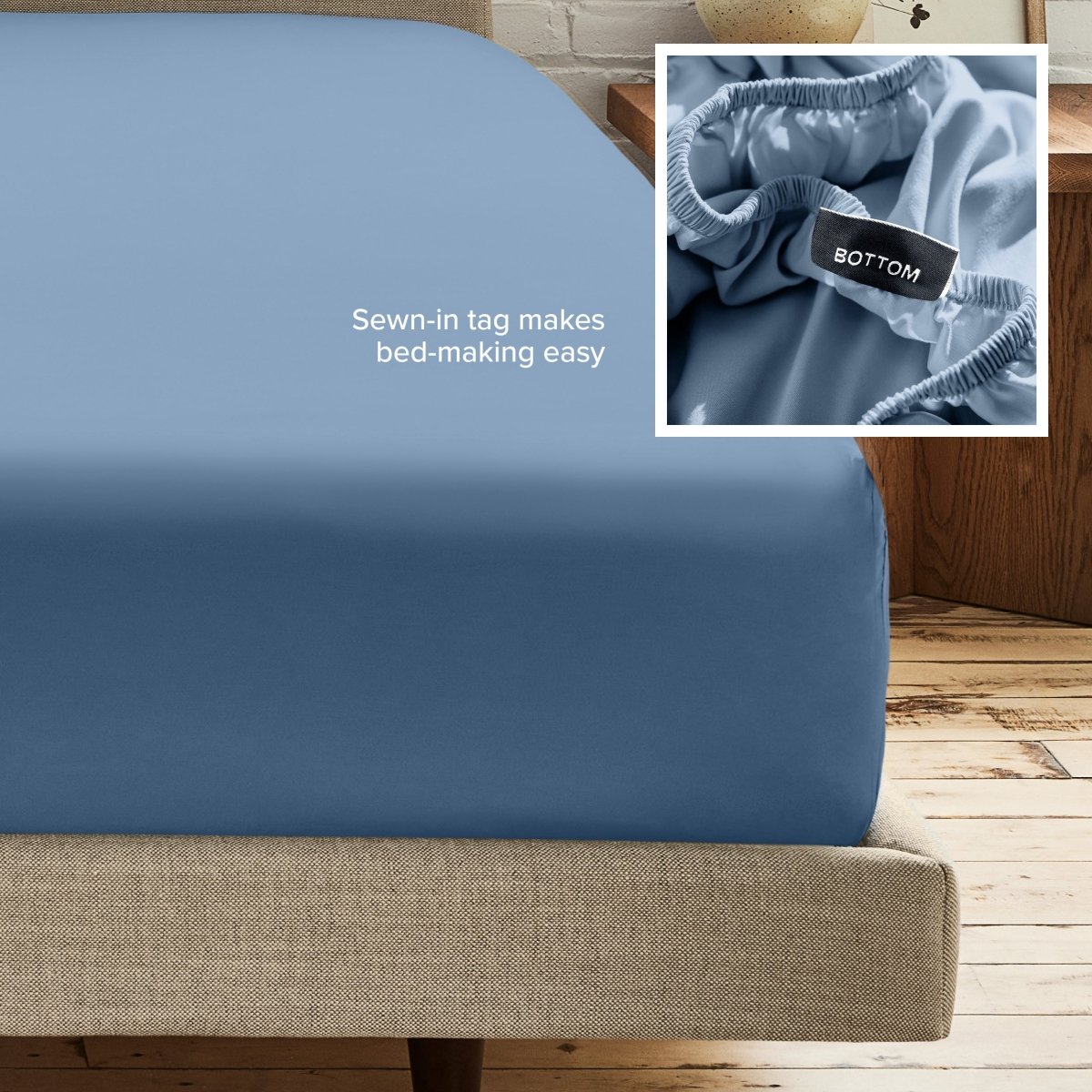 A fitted bed sheet on a bed frame with a small inset close-up of the elastic and a sewn-in tag labeled BOTTOM. White text on the sheet reads, 'Sewn-in tag makes bed-making easy.