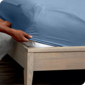 A man is putting a fitted sheet on a mattress