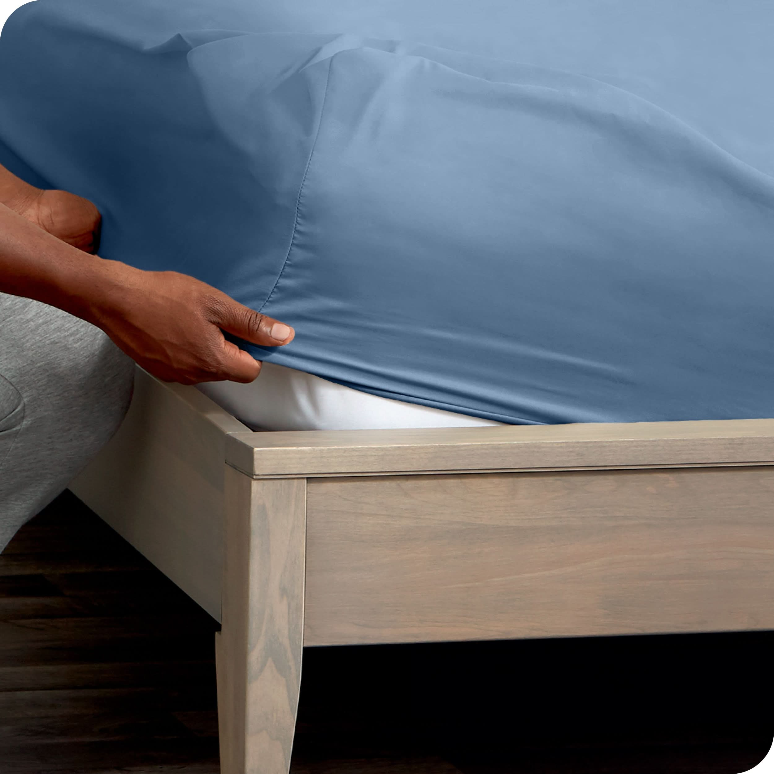 A man is putting a fitted sheet on a mattress