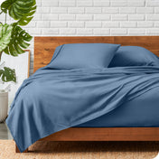 A wooden bed frame with a microfiber sheet set on the mattress.