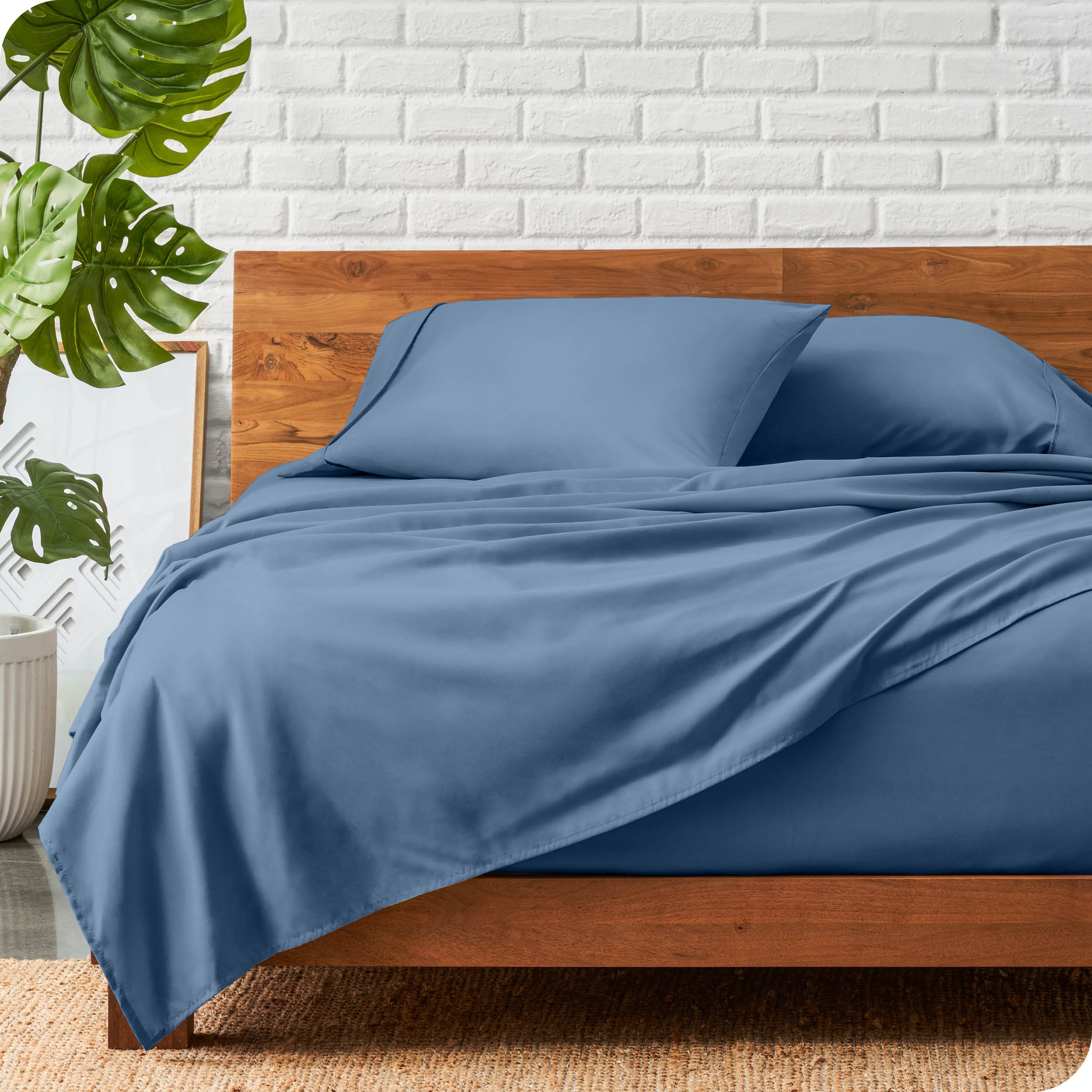 A wooden bed frame with a microfiber sheet set on the mattress.