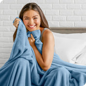 Woman sitting on a bed cuddling with a microplush blanket