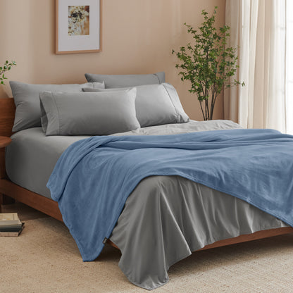 A bed made with grey sheets and a microplush blanket
