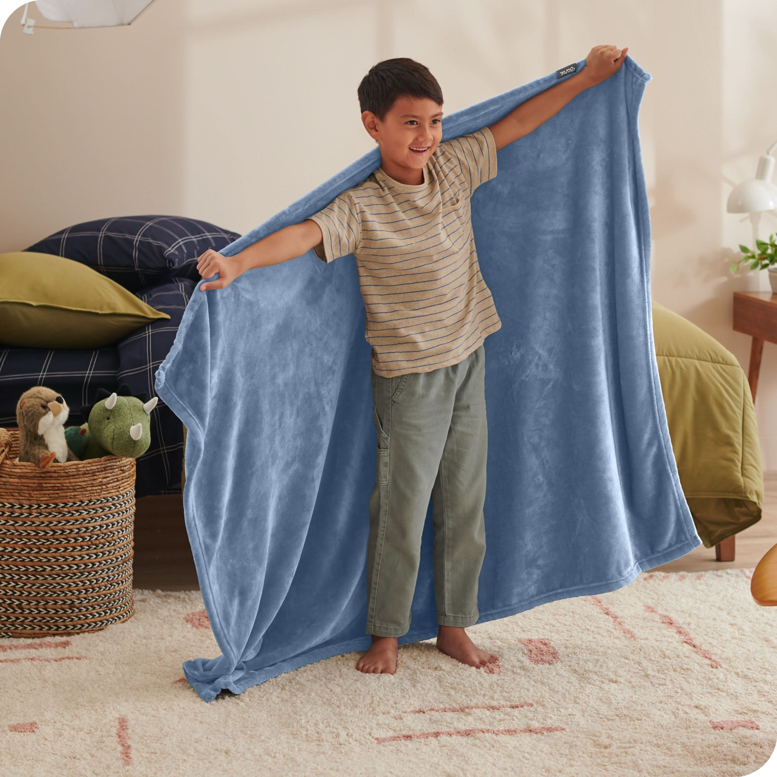 A child has his arms stretched out while holding a microplush blanket behind him